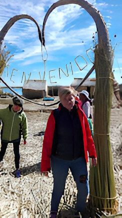 Una mujer con chaqueta roja está de pie junto a un arco de caña que dice 