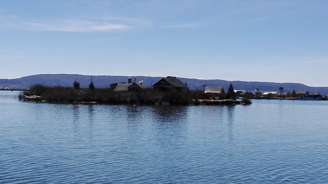 Isla con varios edificios y árboles escasos, en tranquilas aguas azules bajo un cielo despejado.