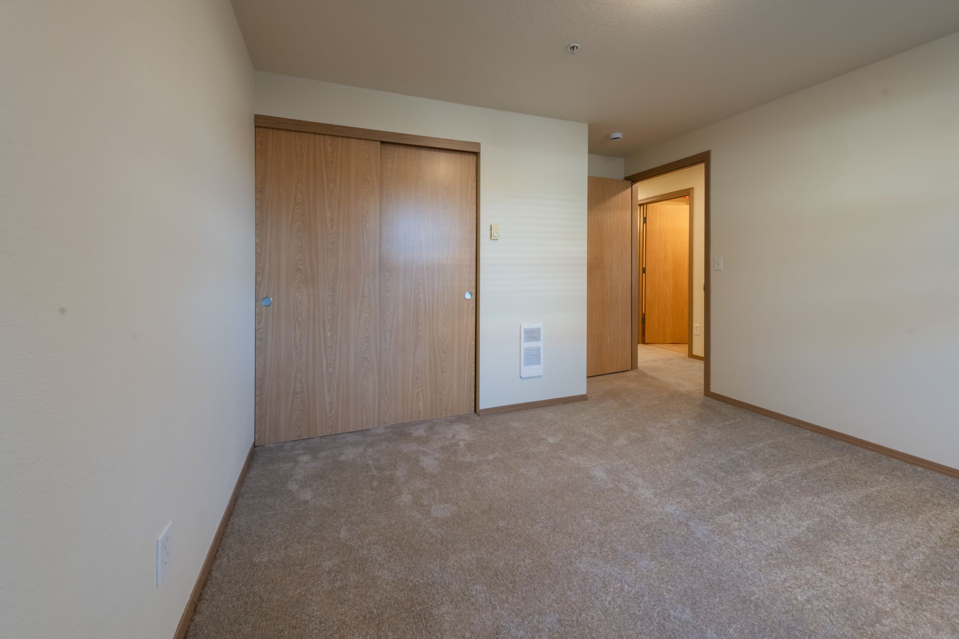 An empty bedroom with a carpeted floor and a closet