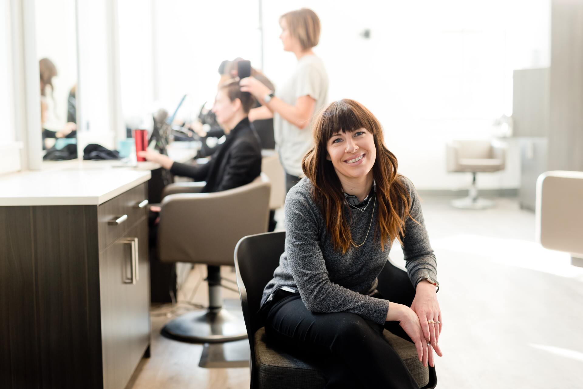 woman in gray long sleeve shirt and black pants sitting on black chair at salon