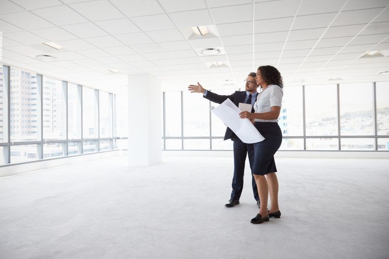 a man and a woman are looking at a blueprint in an empty office