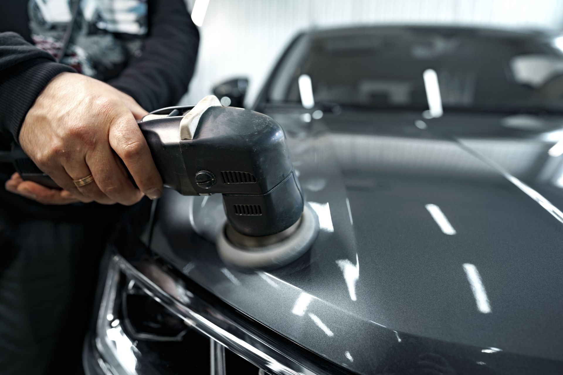 A man is polishing the hood of a car with a machine.