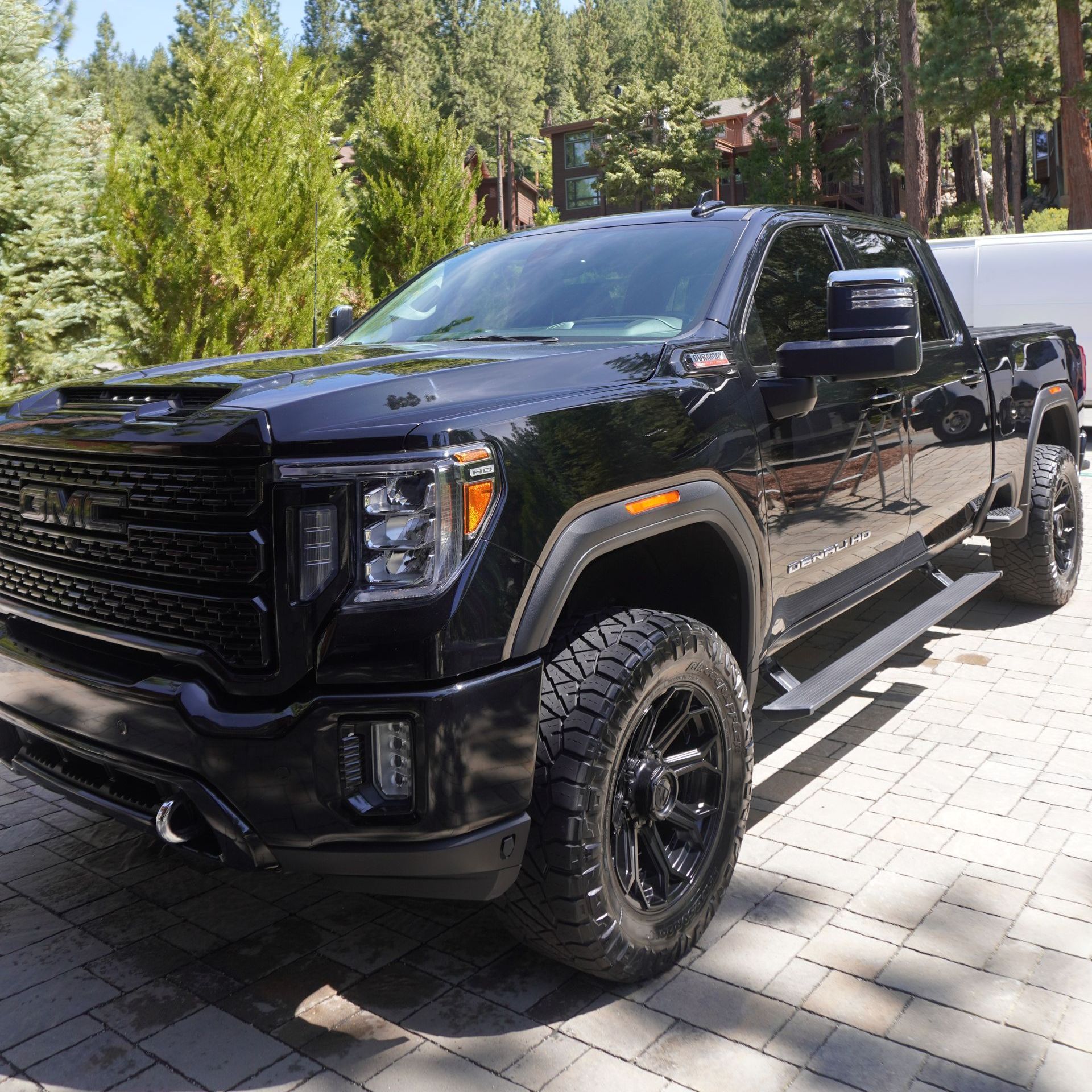 A black truck is parked on a brick driveway in front of a forest.