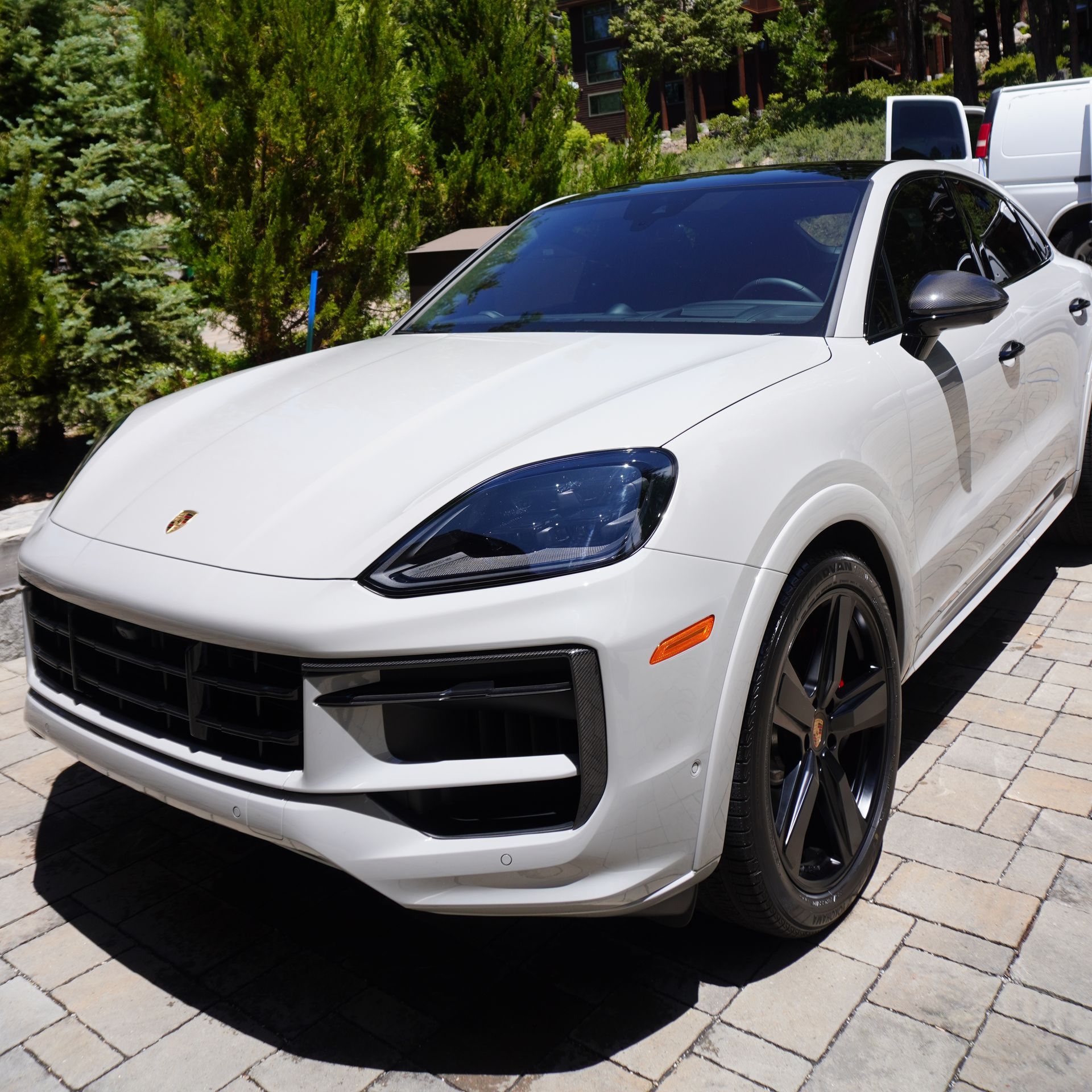A white porsche cayenne is parked on a brick driveway.