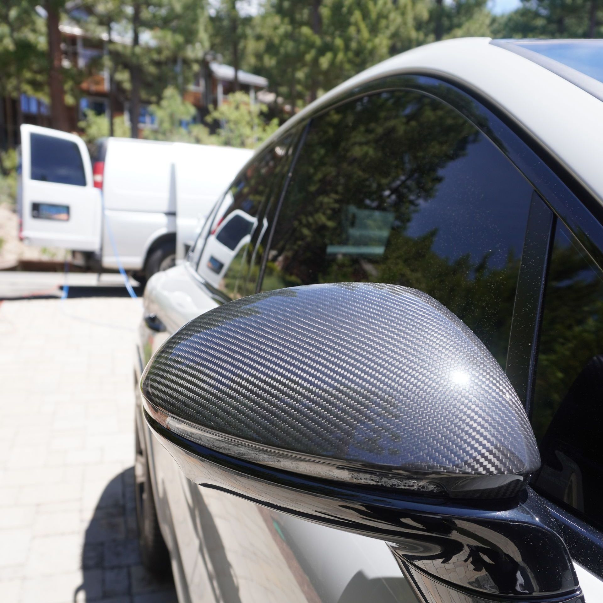 A white car is parked in a driveway with trees in the background.