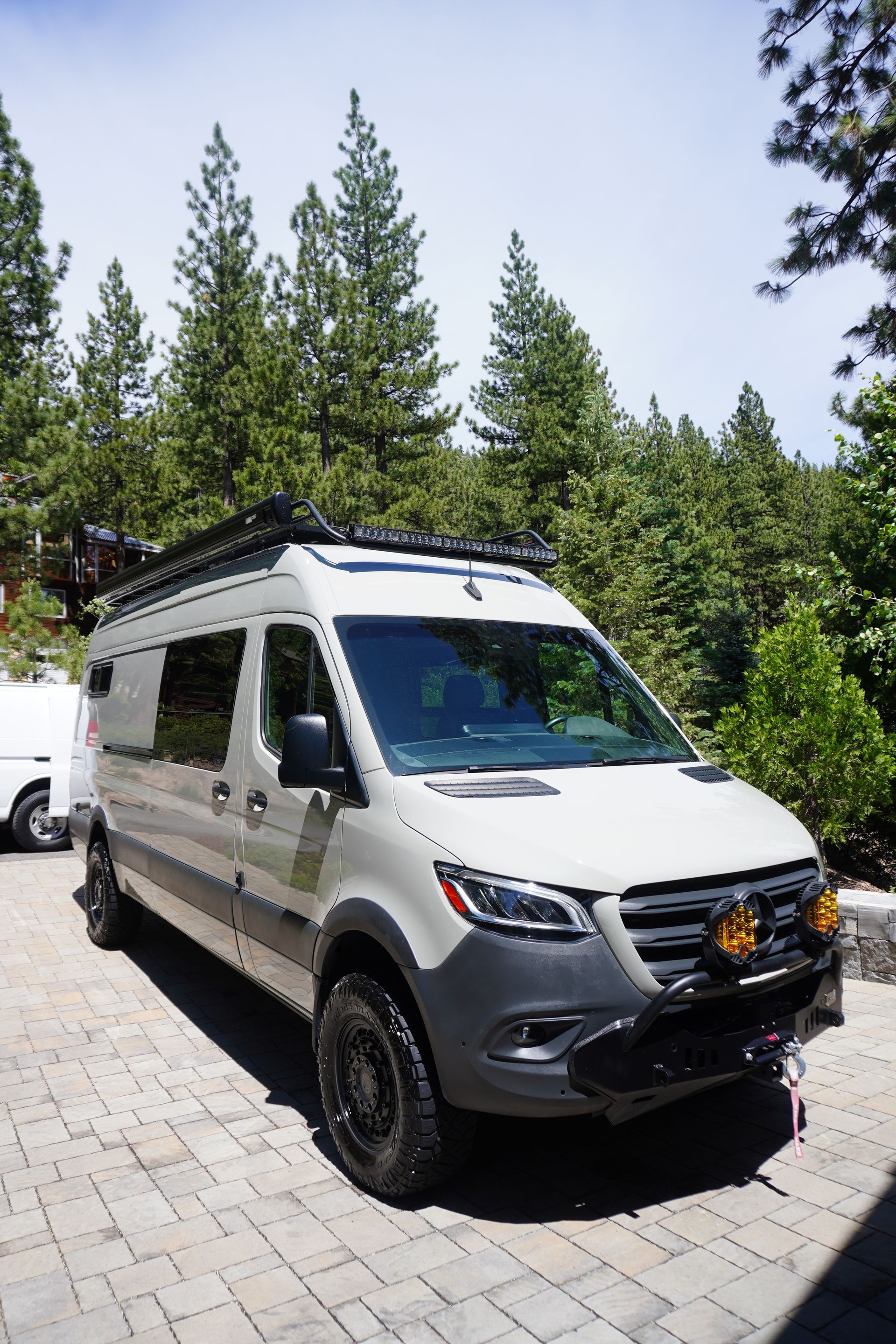 A white van is parked on a brick driveway in front of a forest.