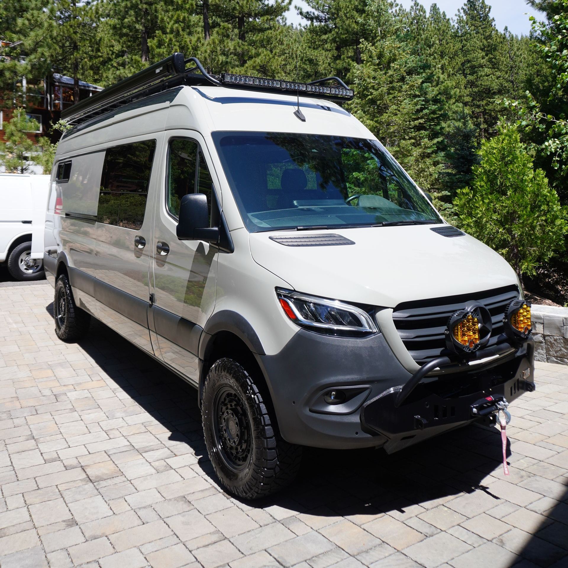 A white van is parked on a brick driveway in front of a forest.