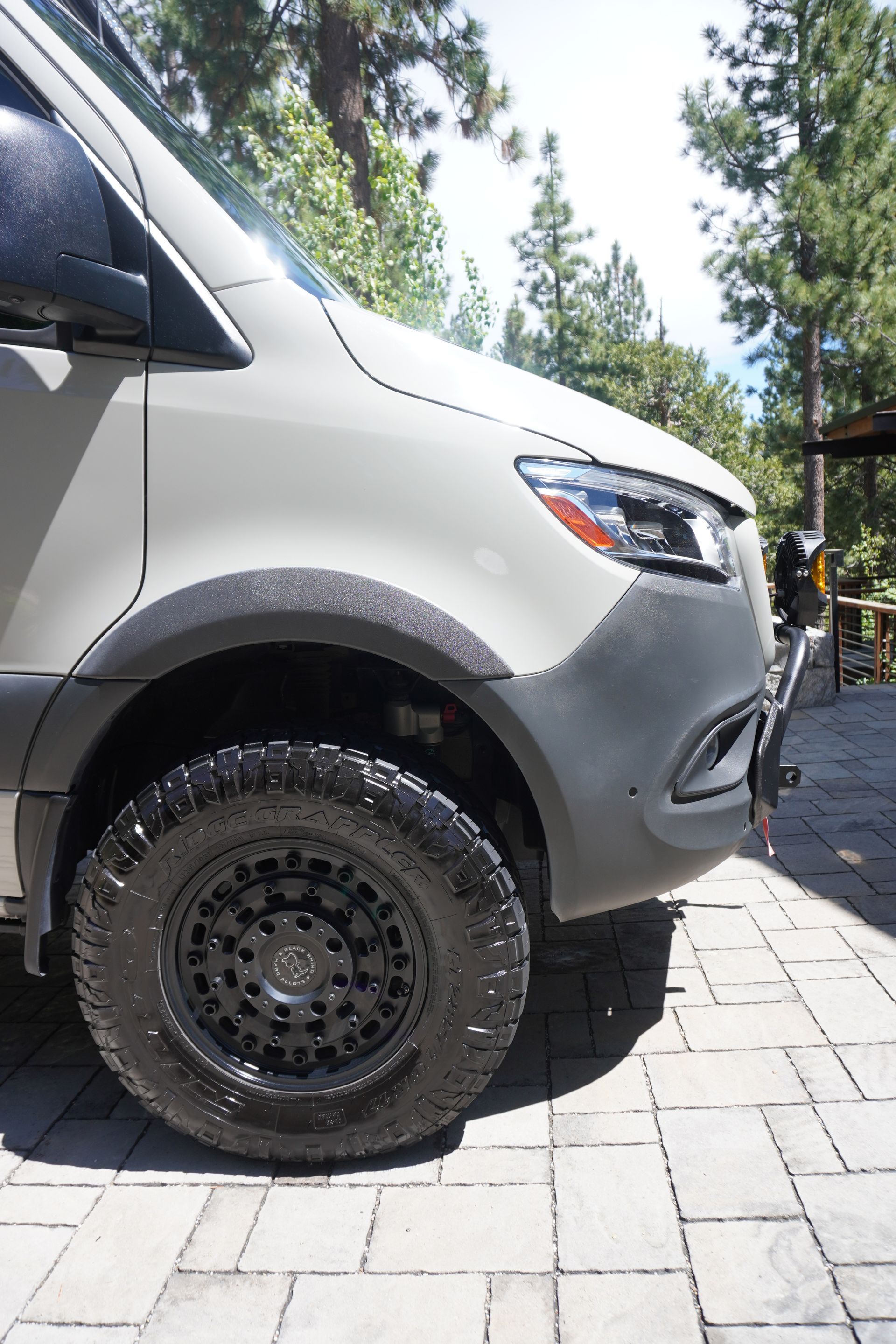 A white van with black tires is parked on a brick driveway.