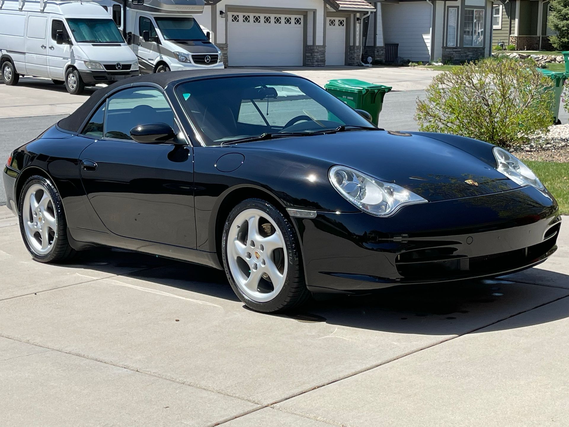 Black Porsche 911 convertible parked on a driveway in front of a house.