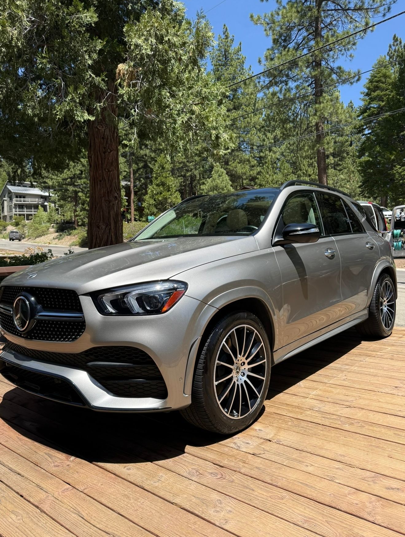Silver Mercedes-Benz GLE SUV parked on a wooden deck, trees in the background under a sunny sky.