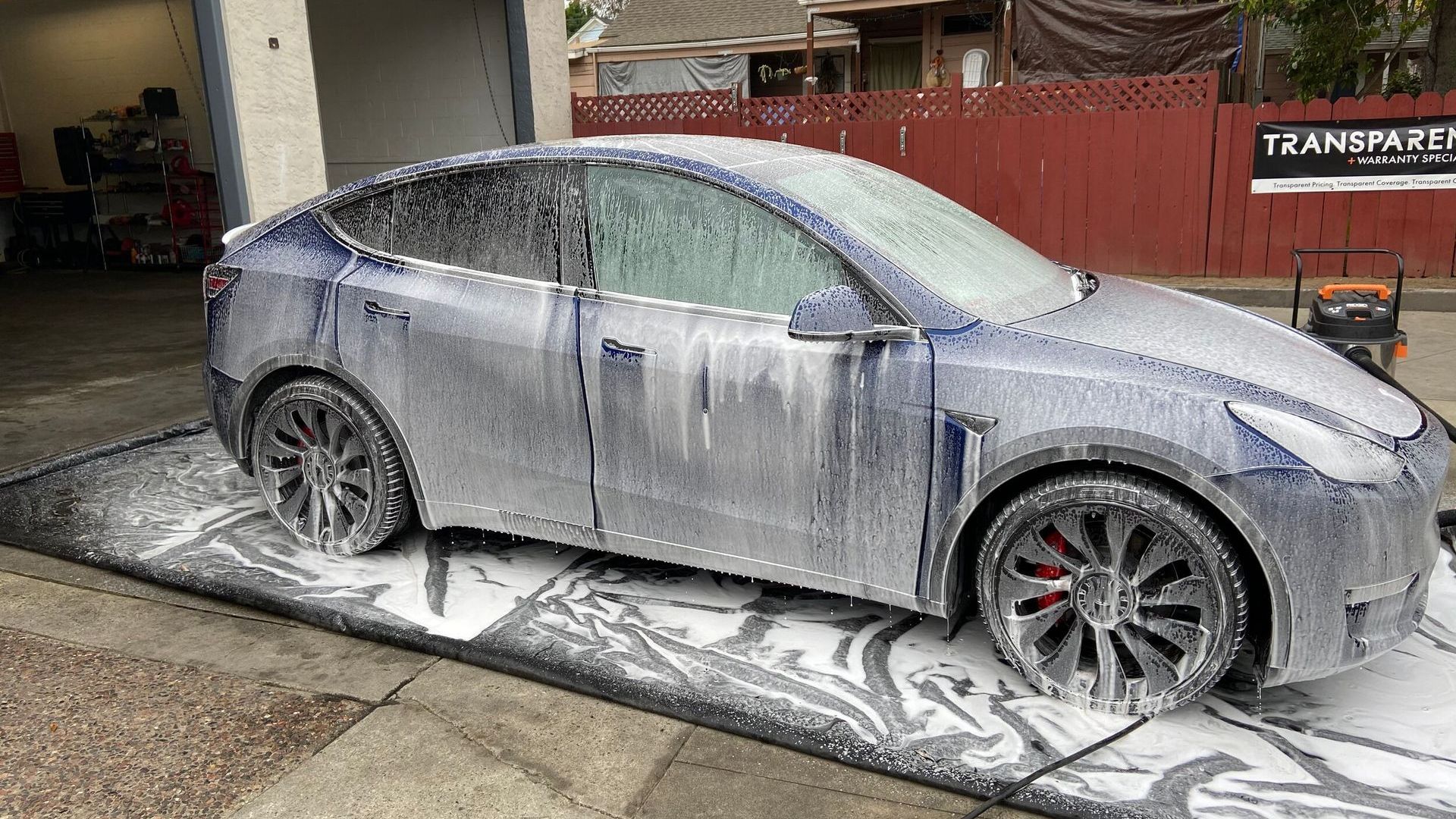 A tesla model y is covered in foam in a driveway.