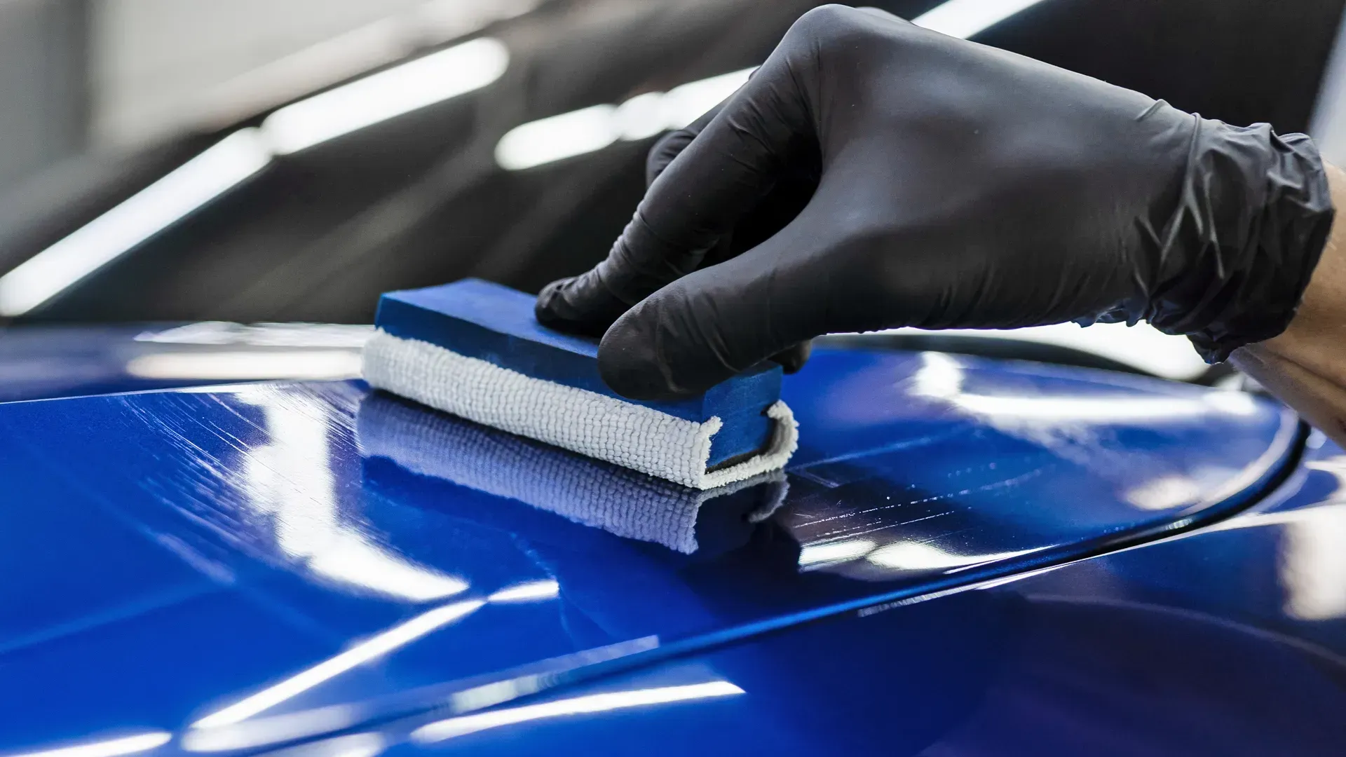 A person is polishing a blue car with a sponge.
