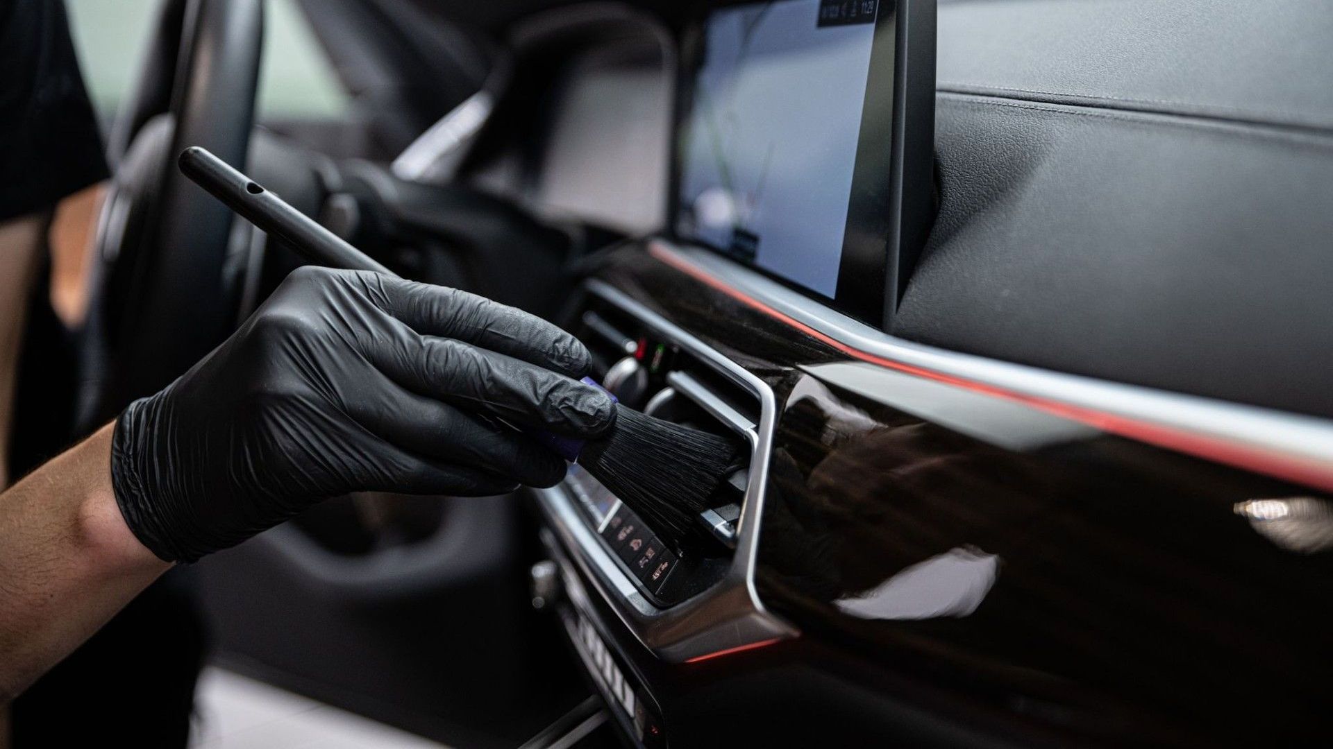 A person wearing black gloves is cleaning the air vents of a car.