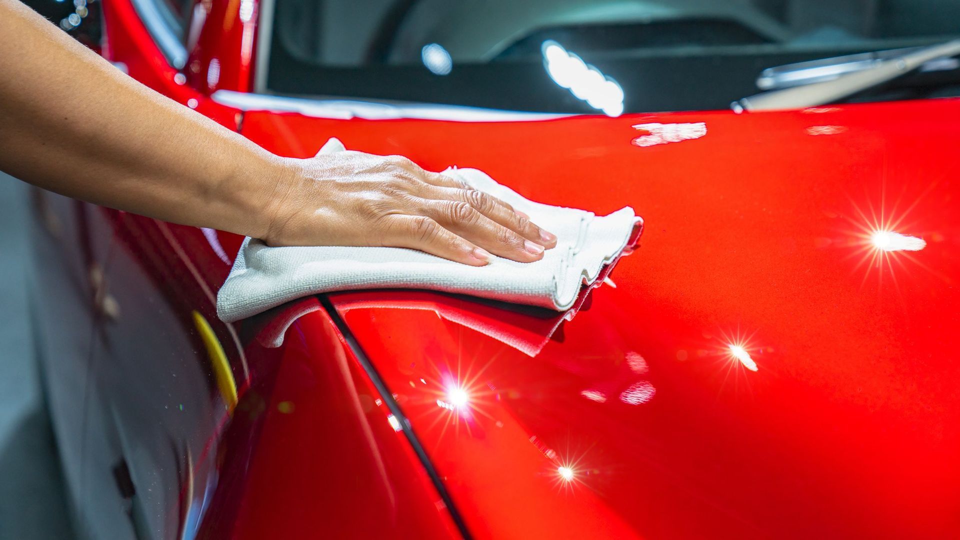 A person is cleaning a red car with a towel.