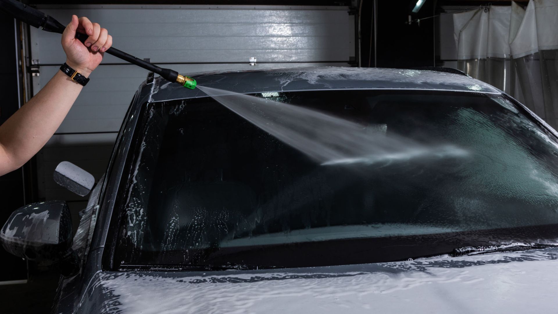 A person is washing a car with a high pressure washer.