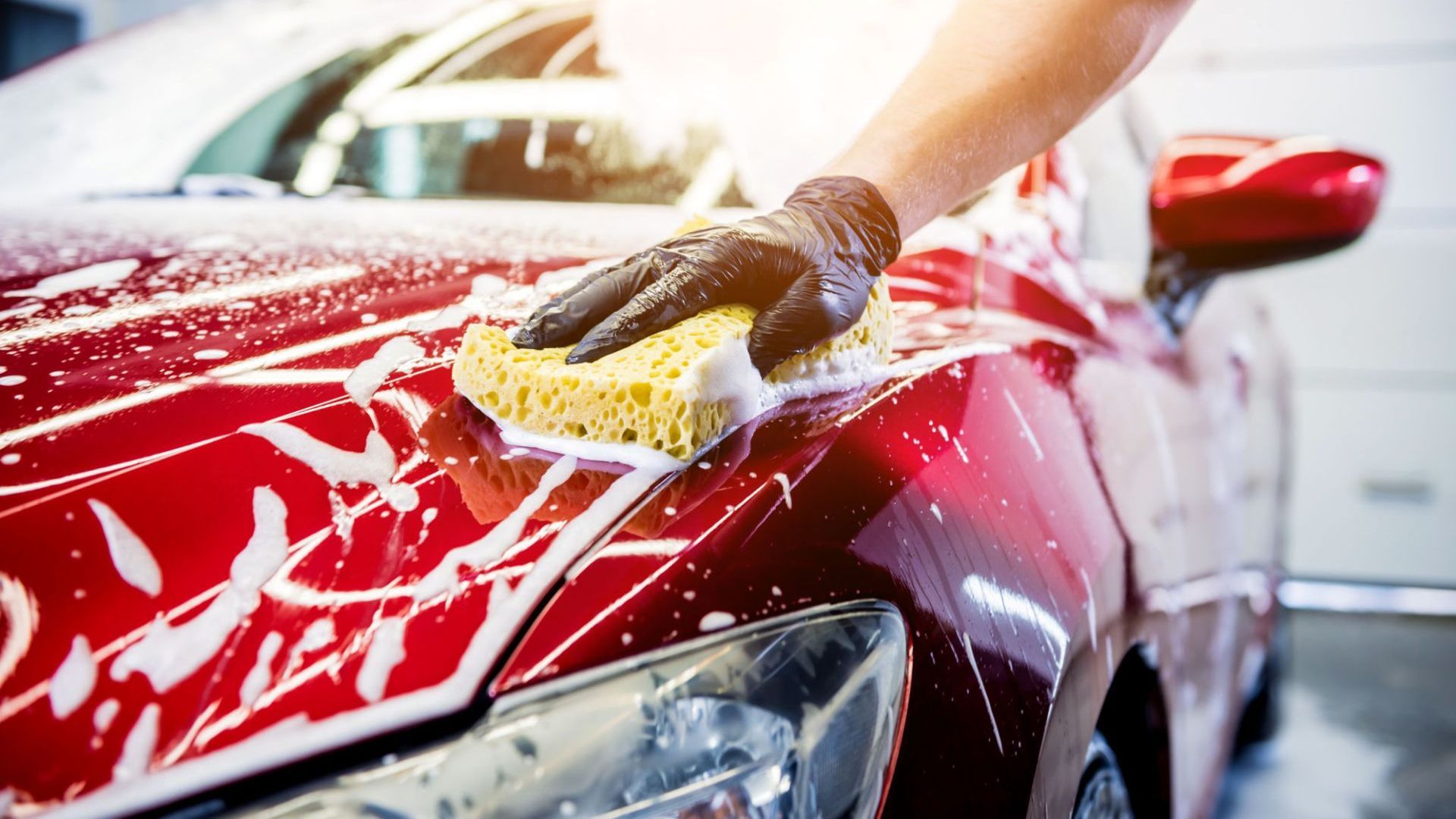 A person is washing a red car with a sponge.
