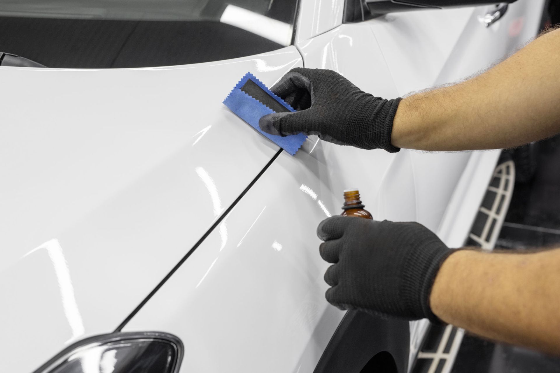 A man wearing black gloves is polishing a white car.