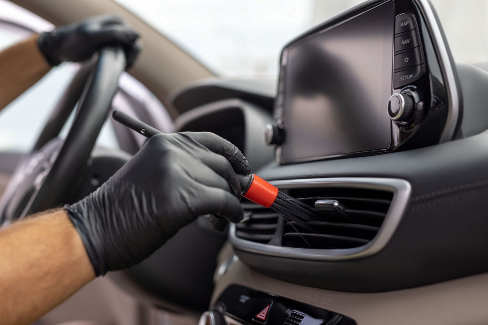 A person is cleaning the air vents of a car with a brush.