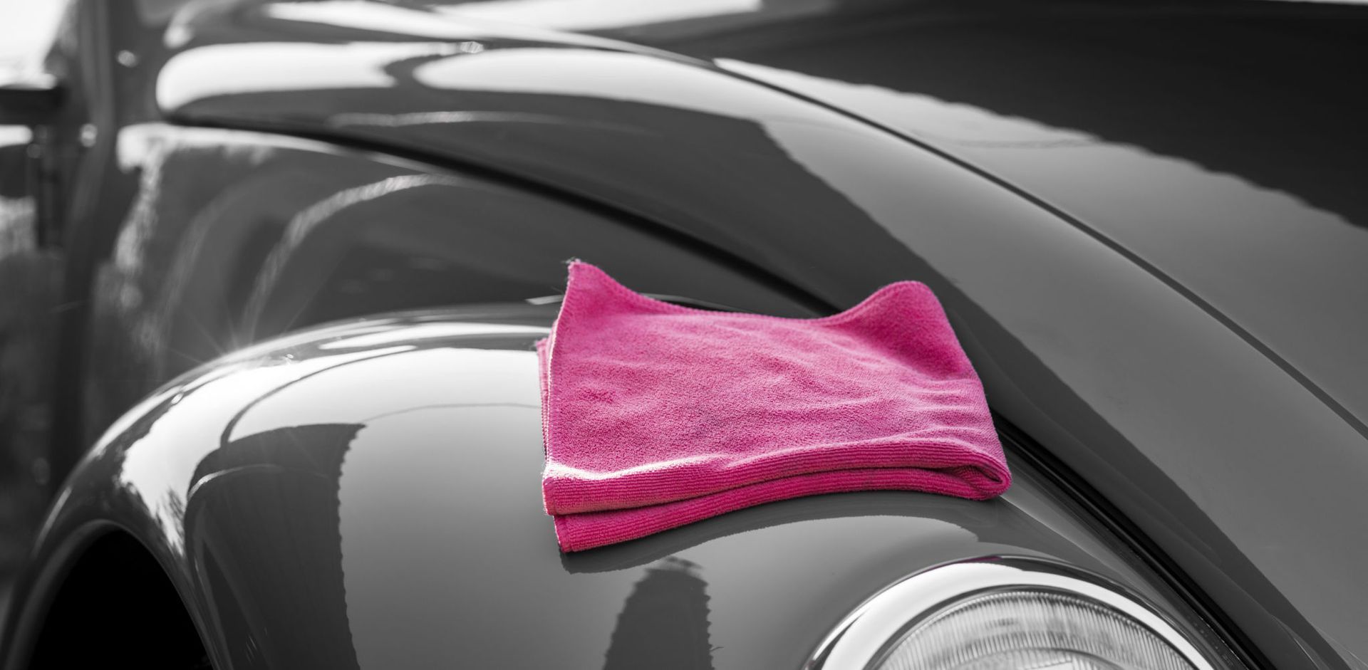 A pink towel is sitting on the hood of a car.