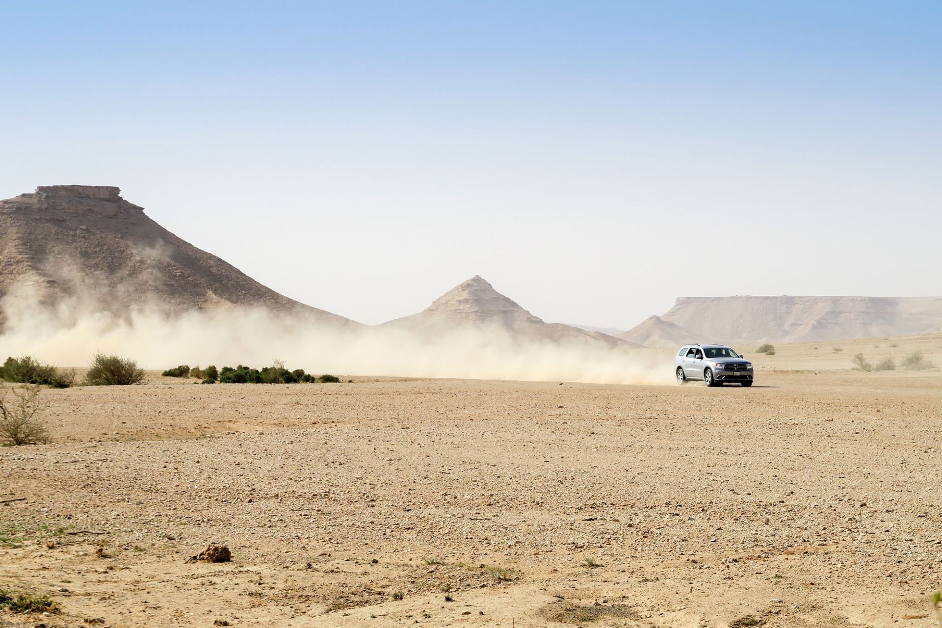 A car is driving through a desert with mountains in the background.