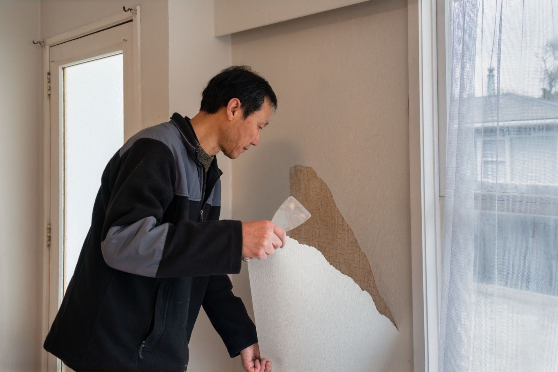 A man is removing wallpaper from a wall with a spatula.