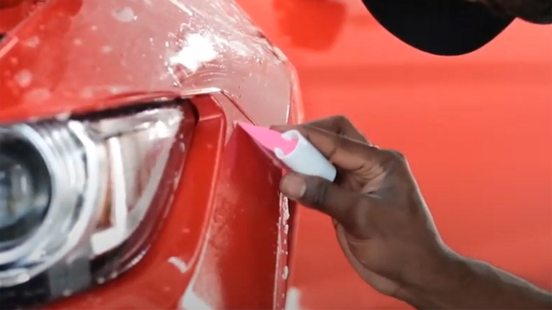 A person is applying a protective film to a red car.