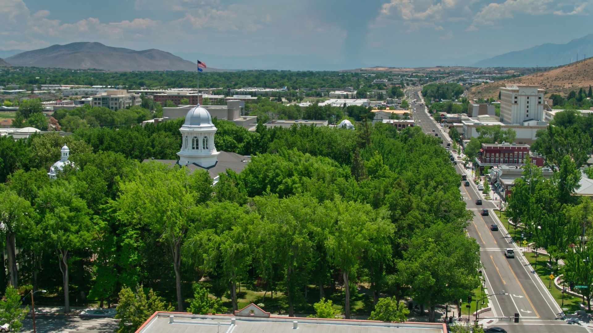 An aerial view of a city with a large white building in the middle of it surrounded by trees.