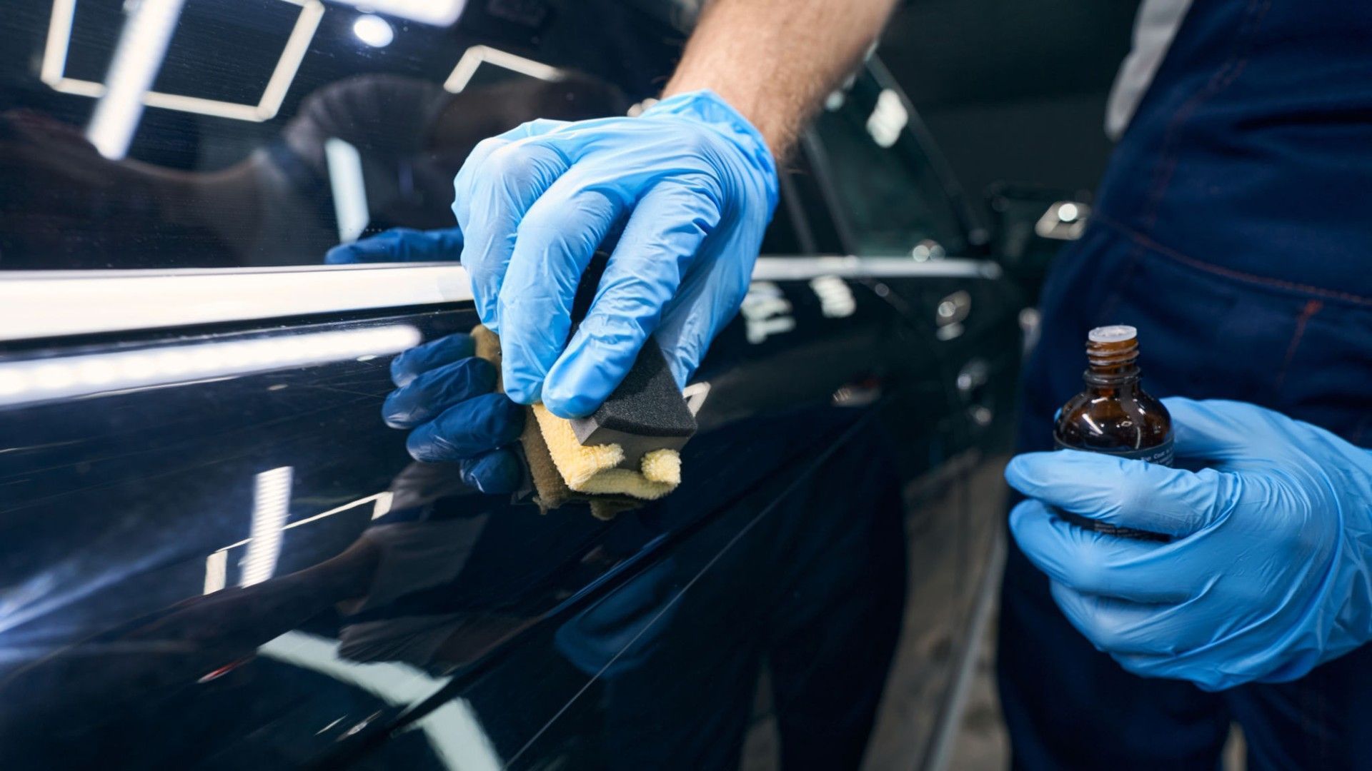 A man wearing blue gloves is polishing a car with a sponge.