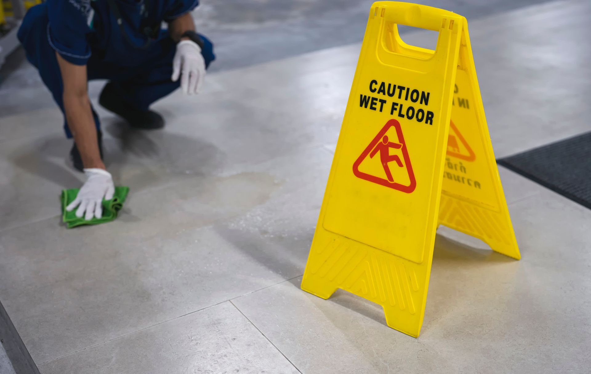 A person is cleaning the floor next to a caution wet floor sign.