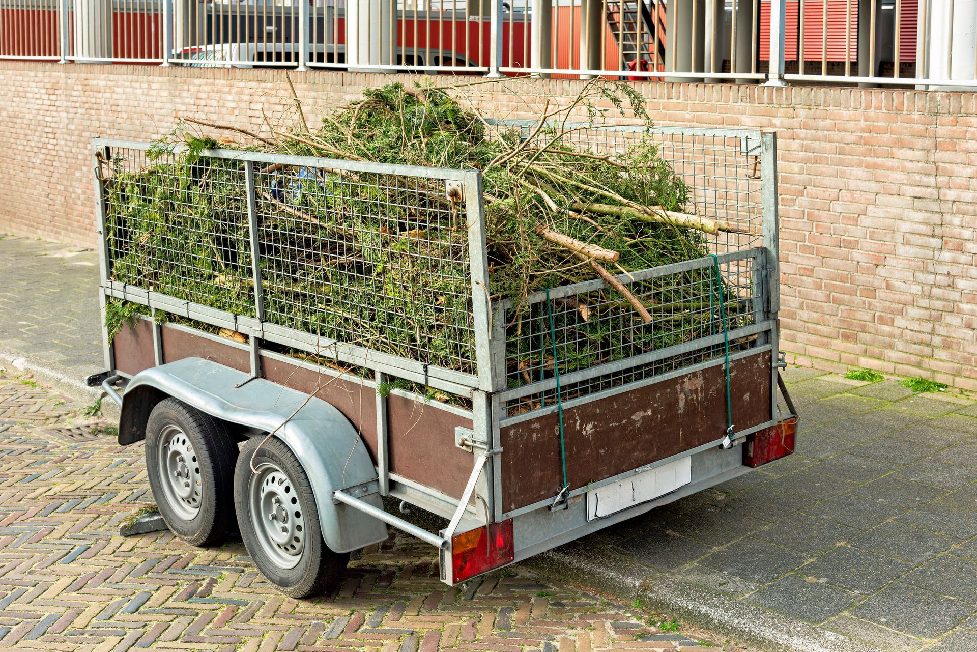 A trailer filled with branches and leaves is parked on the side of the road.