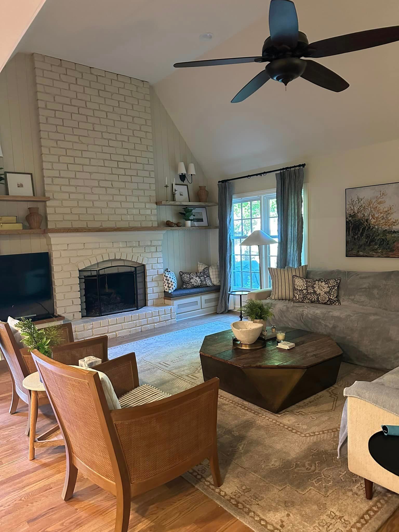 A living room with a fireplace , couch , chairs , coffee table and ceiling fan.