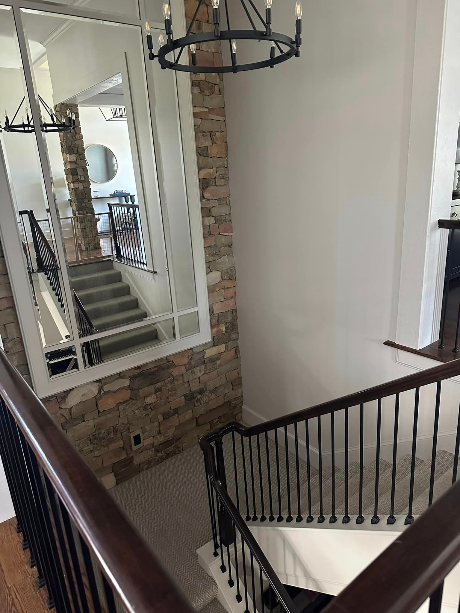 A staircase with a large mirror on the wall and a chandelier hanging from the ceiling.