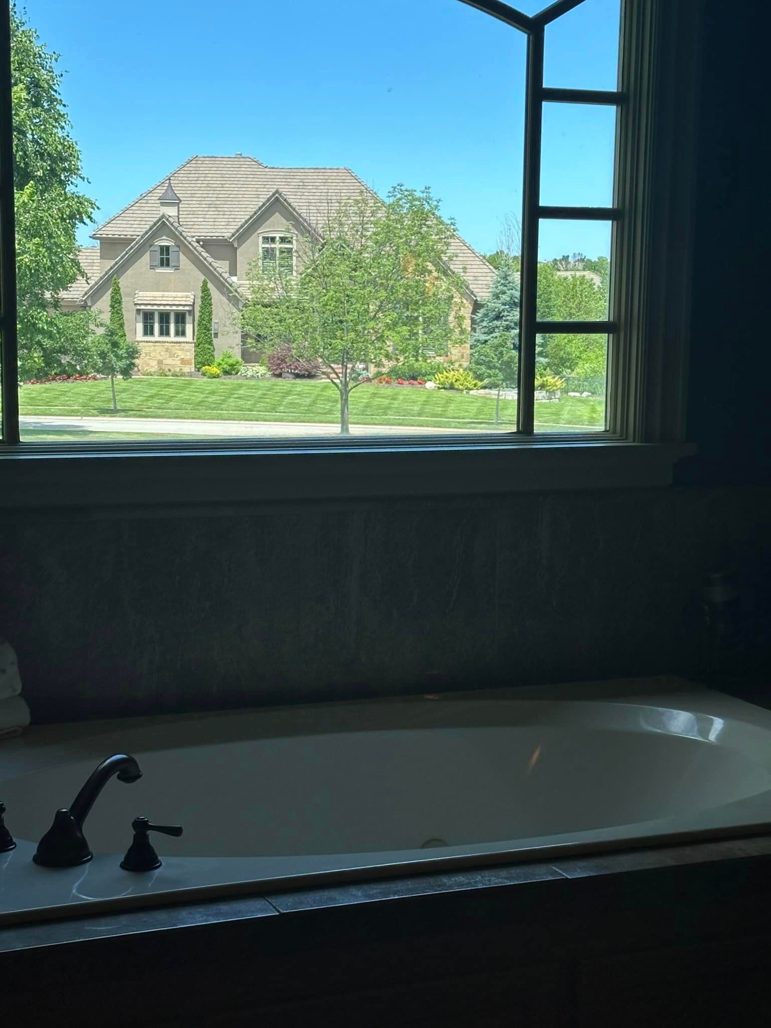 A bathtub with a view of a house through a window