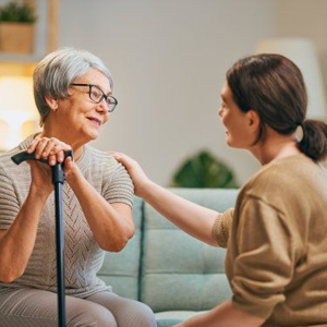 An elderly woman with a cane is sitting on a couch talking to a younger woman.