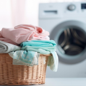 A wicker basket filled with clothes is in front of a washing machine.
