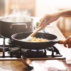 A person is stirring food in a frying pan on a stove