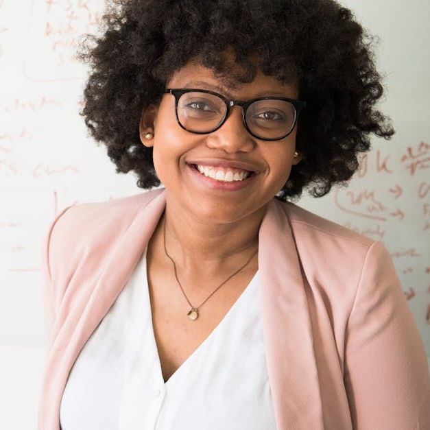 A woman wearing glasses and a pink jacket is smiling