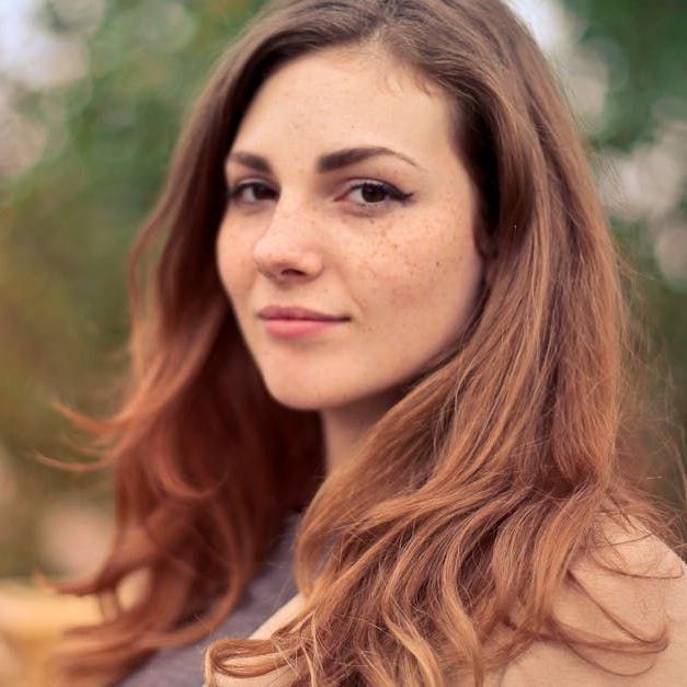 A woman with long red hair and freckles looks at the camera