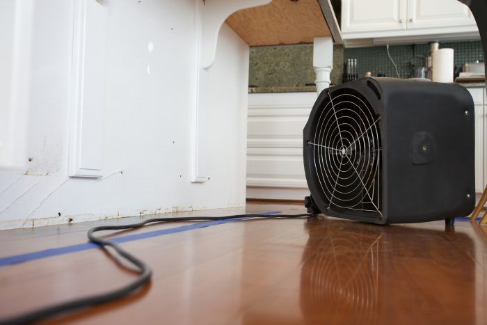 A fan is sitting on a wooden floor in a kitchen.