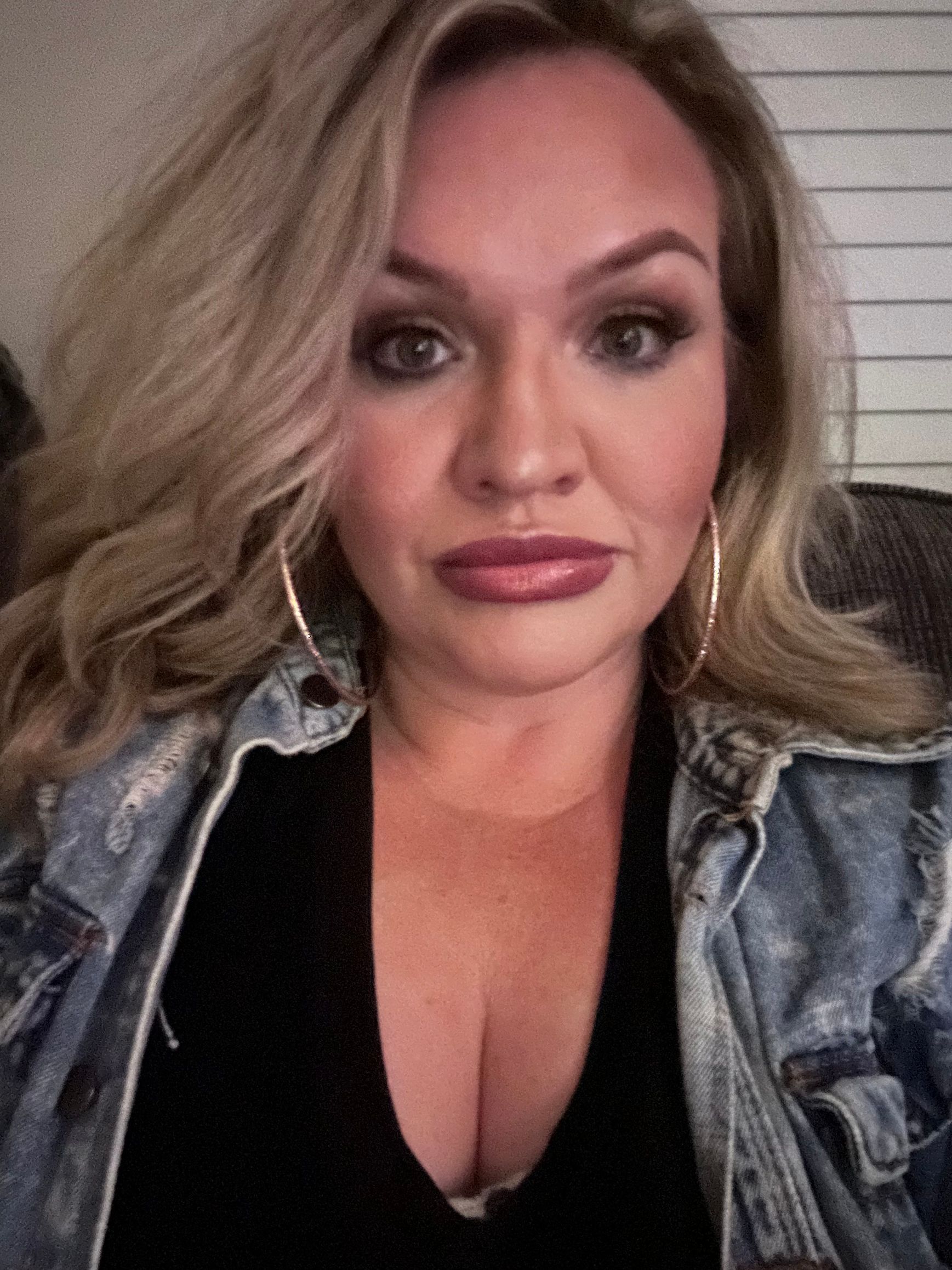 A woman wearing a denim jacket and a black shirt is taking a selfie.