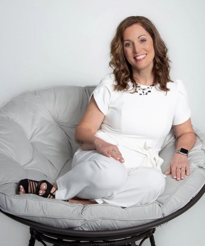 A woman in a white dress is sitting in a chair and smiling.