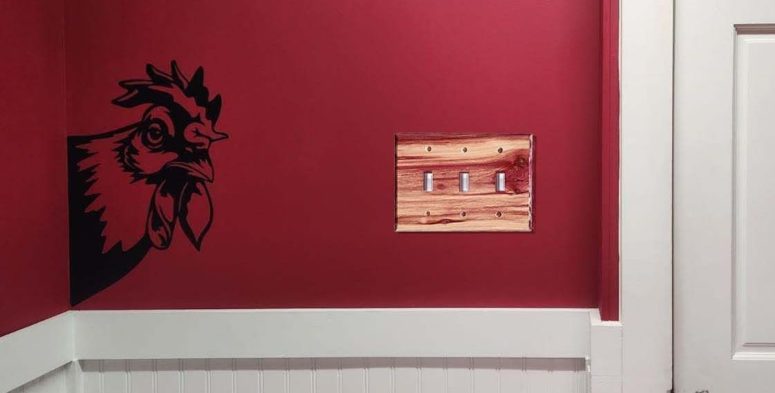 A red wall with a rooster and a traditional wood 3 toggle light switch in traditional juniper.