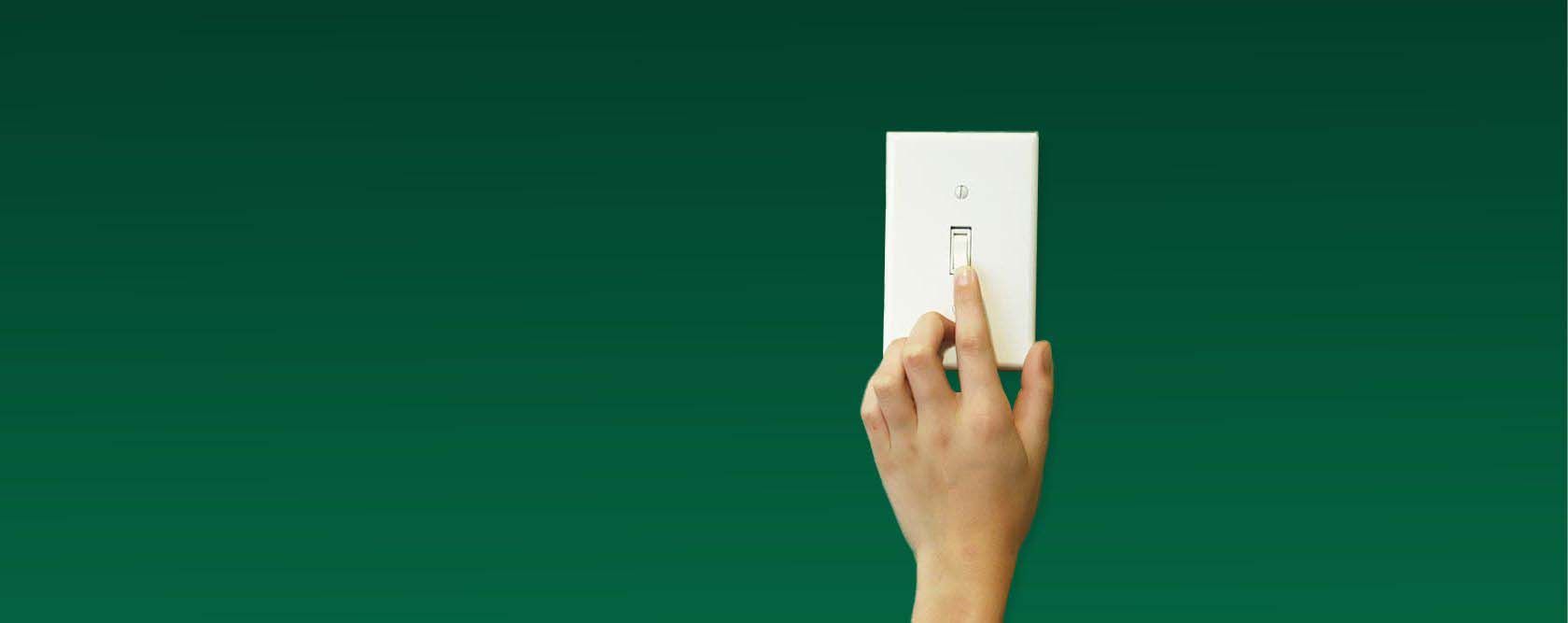 A person 's hand is pressing a light switch on a green wall
