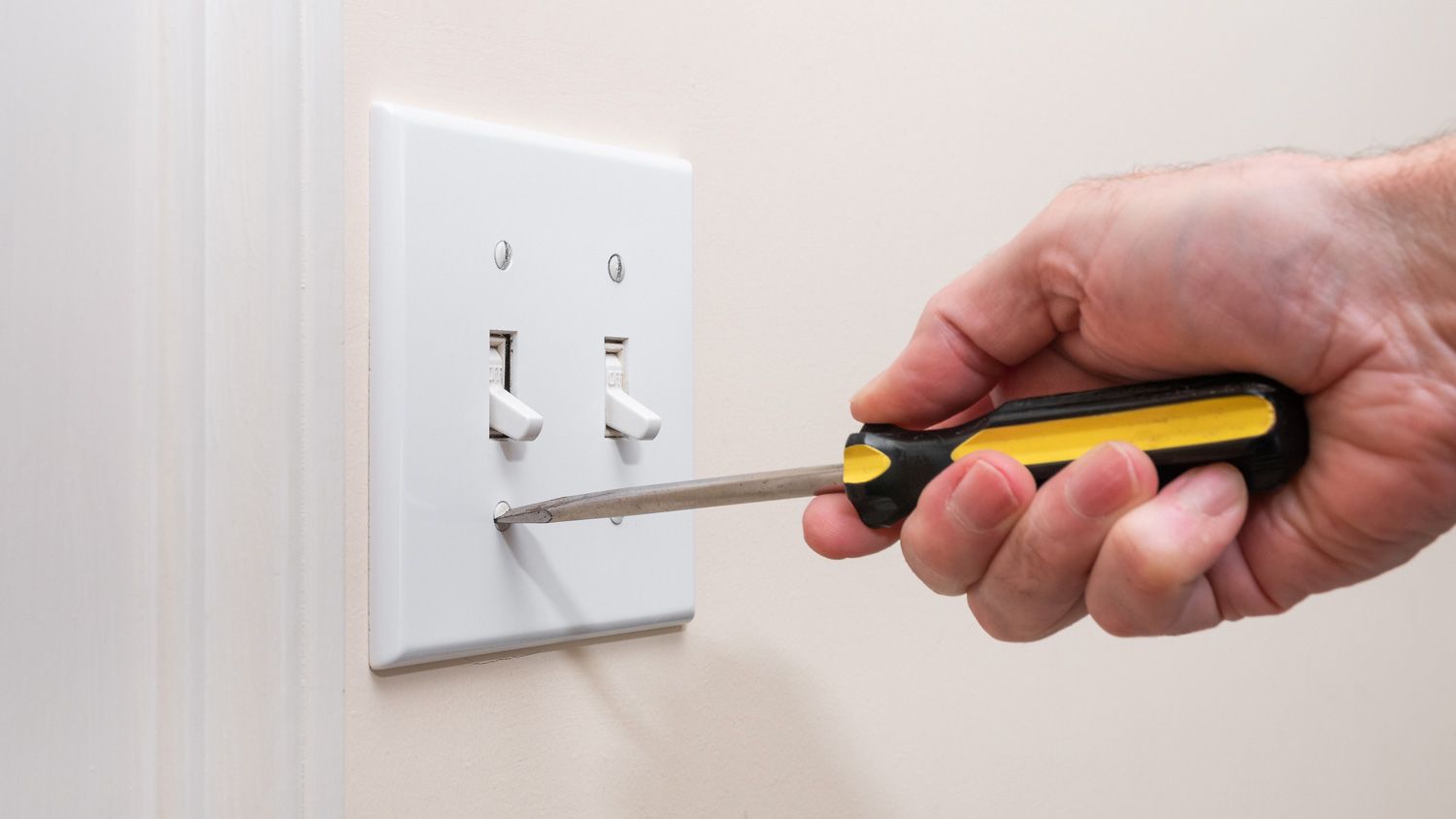 A person is using a screwdriver to remove a light switch.