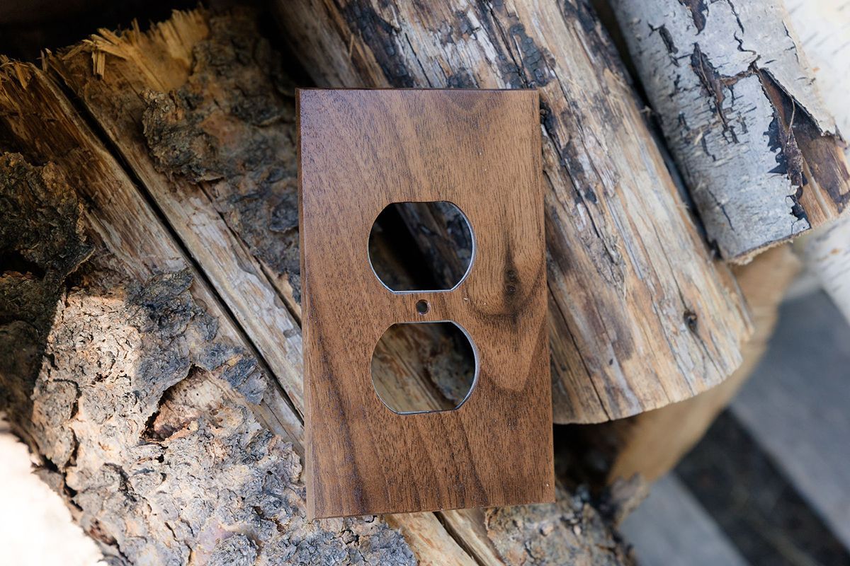 A wooden outlet cover is sitting on top of a pile of logs.