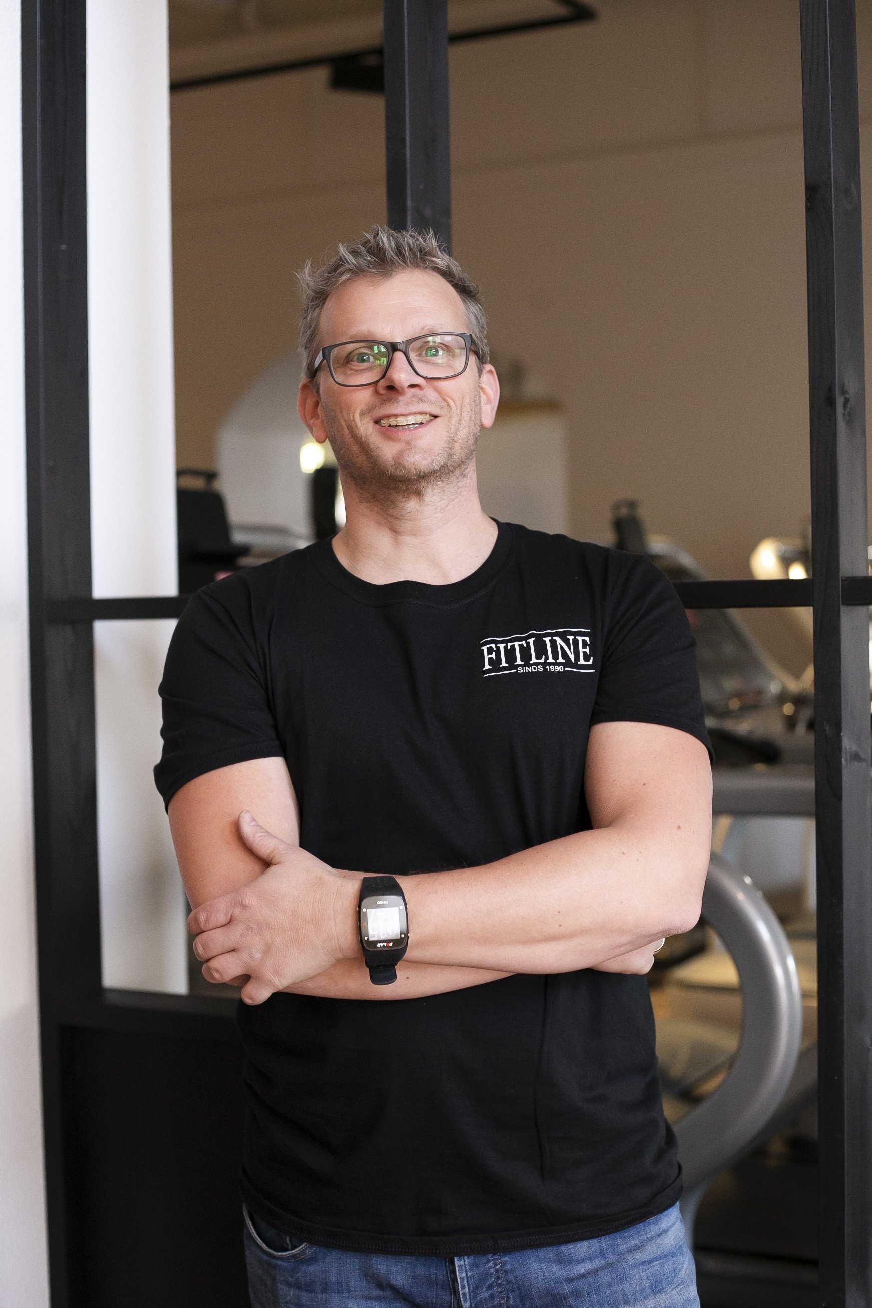 Een man met een bril en een zwart shirt staat met zijn armen over elkaar.