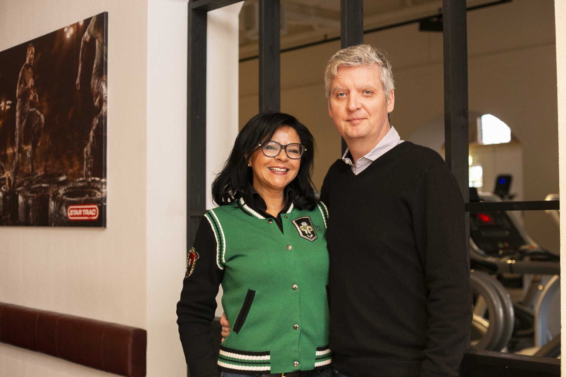 Een man en een vrouw poseren voor een foto in een sportschool.