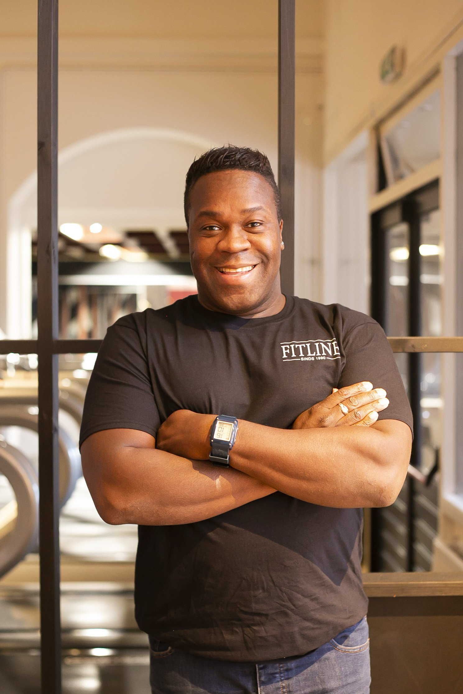 Een man in een zwart shirt staat met zijn armen over elkaar en lacht.