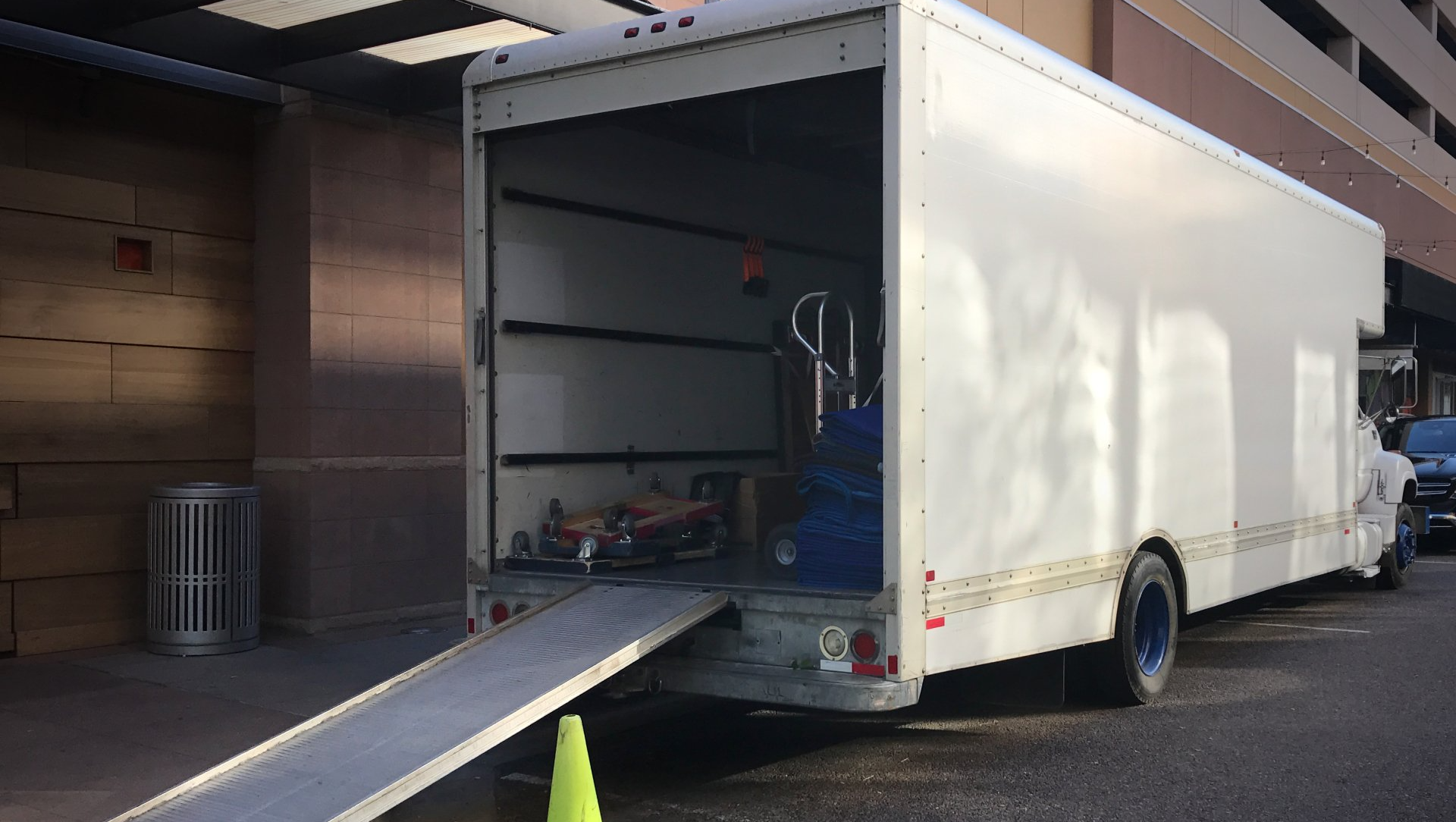 A white moving truck is parked in front of a building with its ramp open.