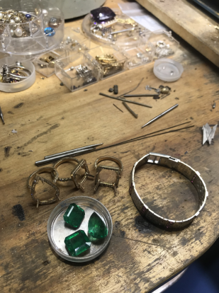 A wooden table with a bracelet and emeralds on it.